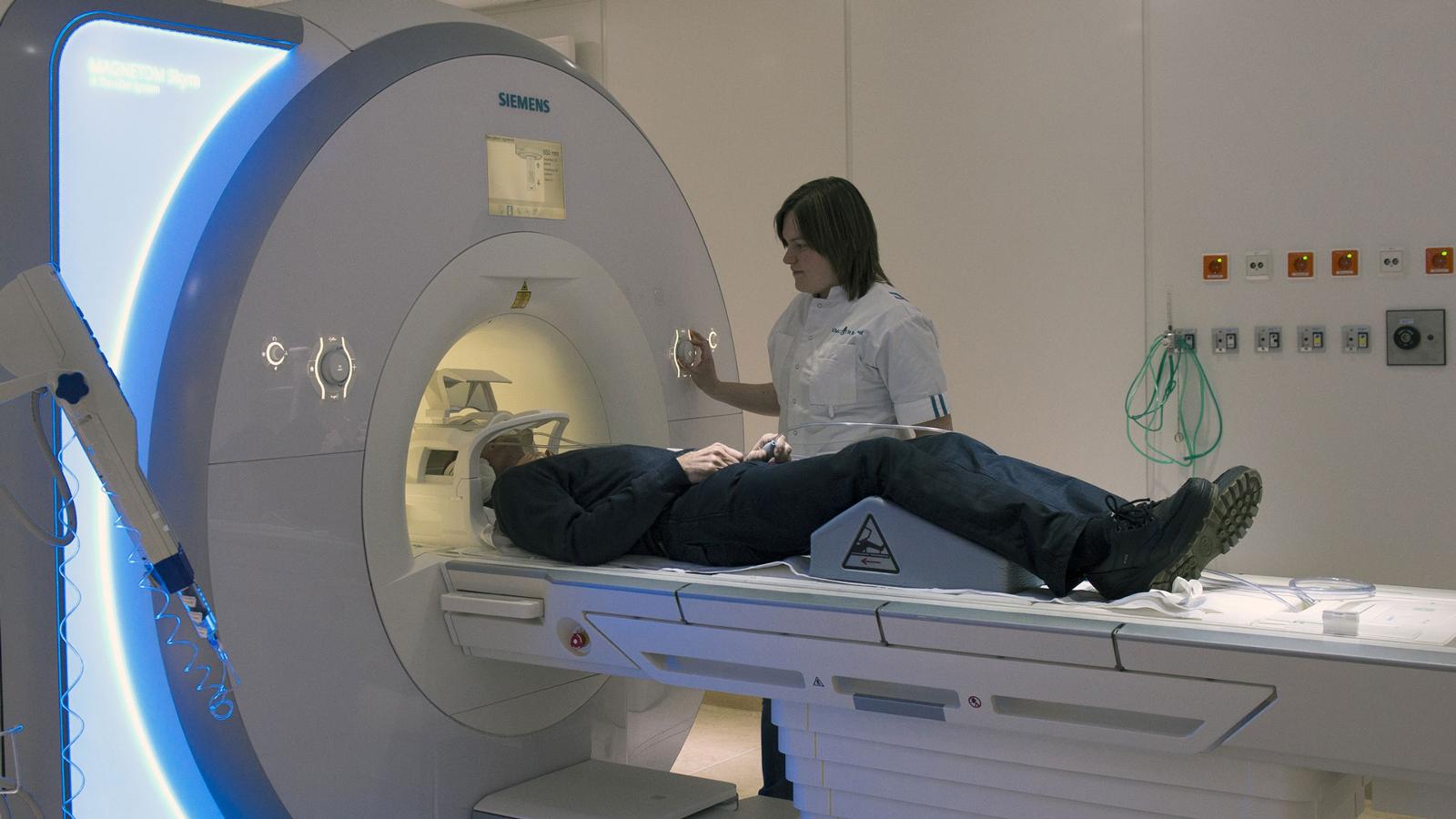 Medisch-specialistische zorg: Radiologe helpt patiënt die met hoofd in MRI-scanner moet
