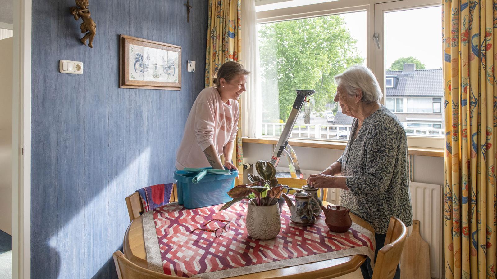 Wijkverpleging: Huishoudelijke thuiszorgmedewerkster maakt praatje in huis cliënt