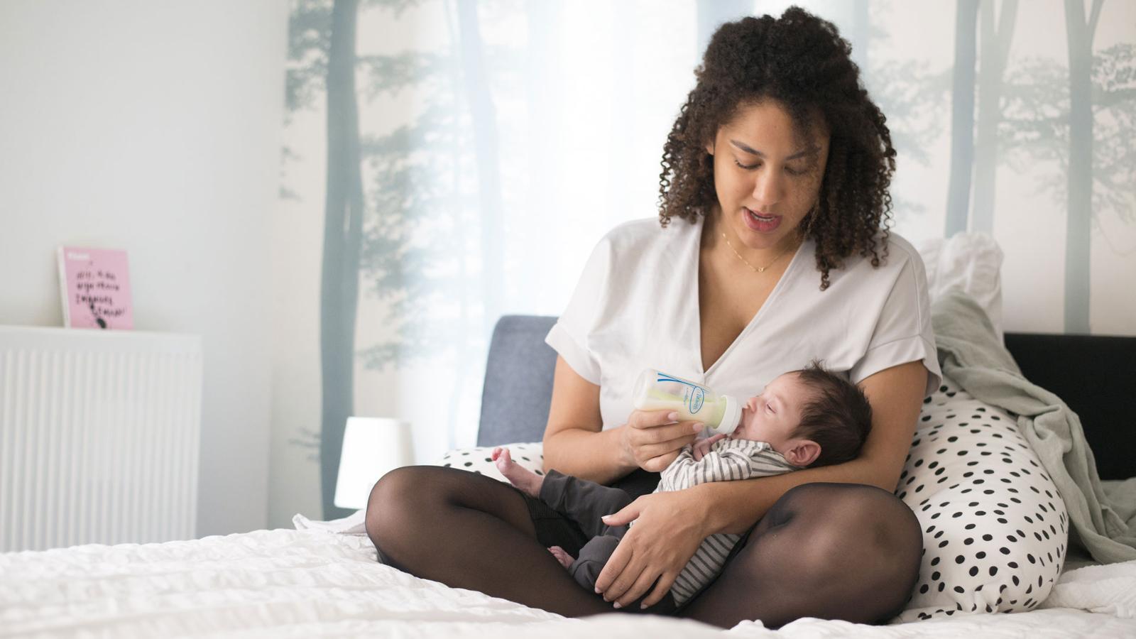 Kraamzorg: Jonge moeder geeft baby op schoot de fles